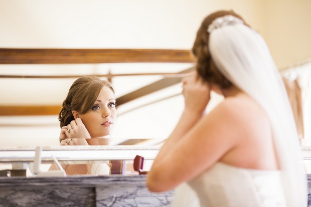 bride putting on earrings in mirror