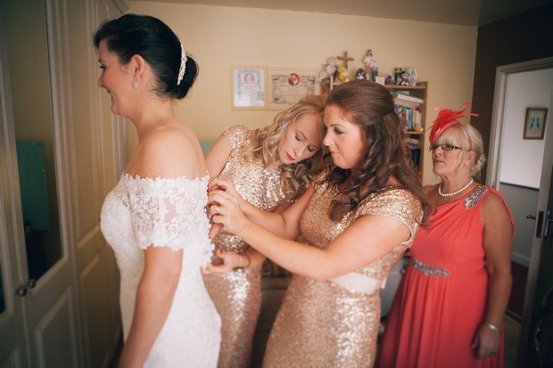 bridesmaid-buttoning-up-bride's-dress-wedding-morning