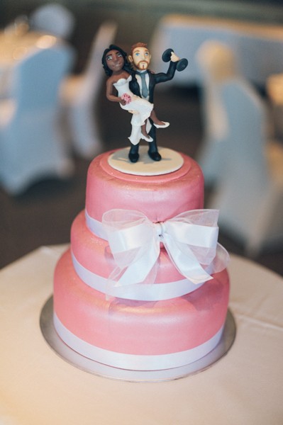 pink wedding cake with white bow and bride and groom cake topper