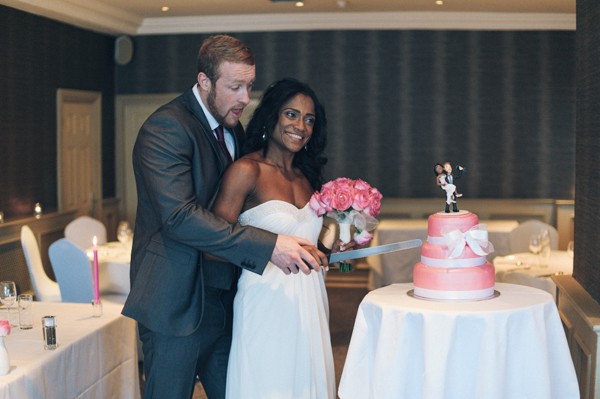 bride and groom smiling and cutting pink wedding cake
